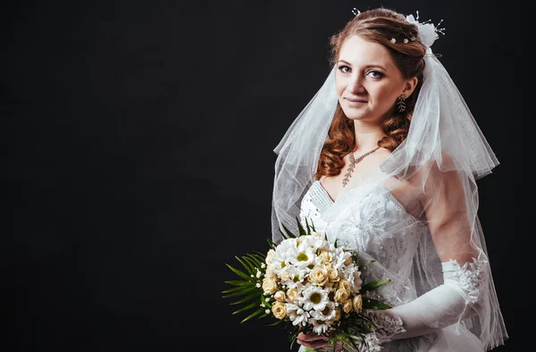 Modèle de mode avec bouquet nuptial buvant du champagne et portant une robe de mariée à fond noir studio — Photo