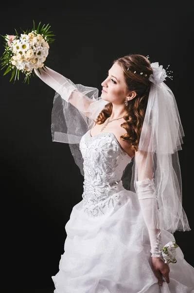 Modelo de moda com buquê de noiva bebendo champanhe e vestindo vestido de noiva no fundo do estúdio preto — Fotografia de Stock