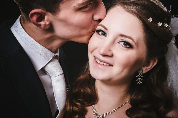 Bruden och brudgummen kyssar, kramar. bröllopsfoto taget i studion på svart bakgrund — Stockfoto