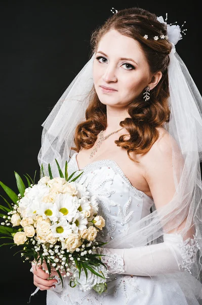 Modèle de mode avec bouquet nuptial buvant du champagne et portant une robe de mariée à fond noir studio — Photo
