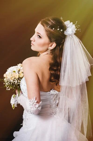 Fashion model with bridal bouquet drinking champagne and wearing wedding dress at black studio background — Stock Photo, Image