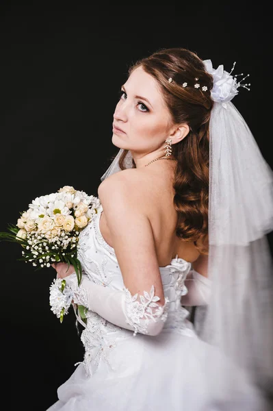 Modella con bouquet da sposa bere champagne e indossare abito da sposa su sfondo nero studio — Foto Stock