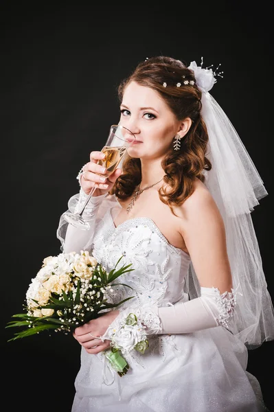 Modelo de moda com buquê de noiva bebendo champanhe e vestindo vestido de noiva no fundo do estúdio preto — Fotografia de Stock