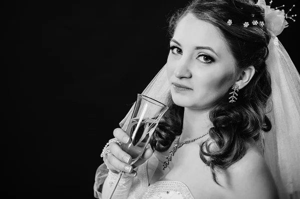 Модная модель со свадебным букетом, пьющая шампанское и одетая в свадебное платье на фоне черной студии — стоковое фото