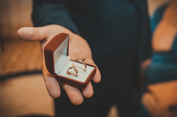 Groom detém uma caixa de presente de jóias com anéis de casamento de ouro. Homem de terno e gravata segurando anel de noivado — Fotografia de Stock