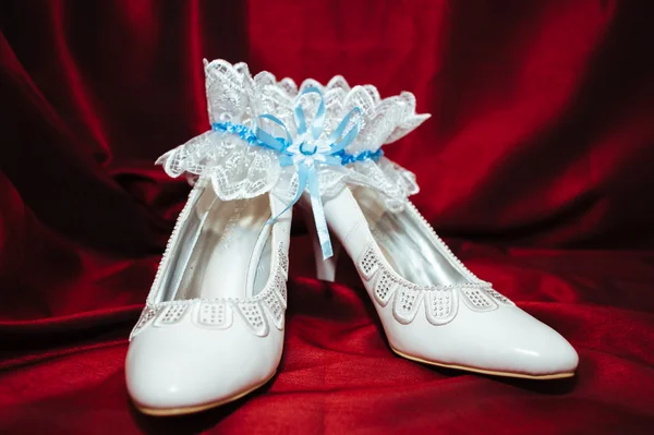 Luxus-Hochzeitsschuhe. elegante Brautschuhe und ein weißes Strumpfband auf rotem Hintergrund. — Stockfoto