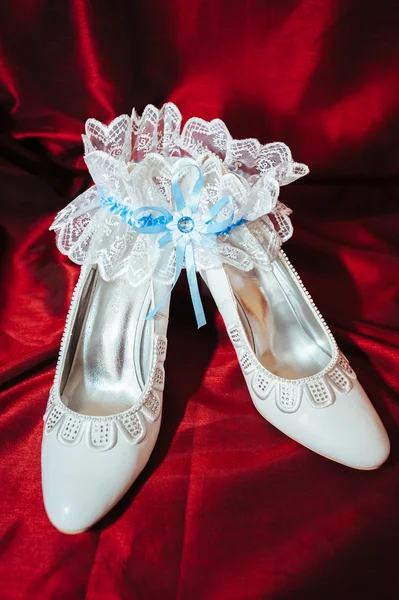 Luxus-Hochzeitsschuhe. elegante Brautschuhe und ein weißes Strumpfband auf rotem Hintergrund. — Stockfoto