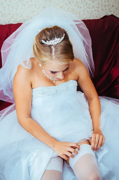 Giarrettiera sulla gamba della sposa, sottile sposa sexy in abito da sposa di lusso mostrando la sua giarrettiera di seta con nastro dorato. donna hanno preparazione finale per la cerimonia nuziale. Momenti del giorno del matrimonio — Foto Stock