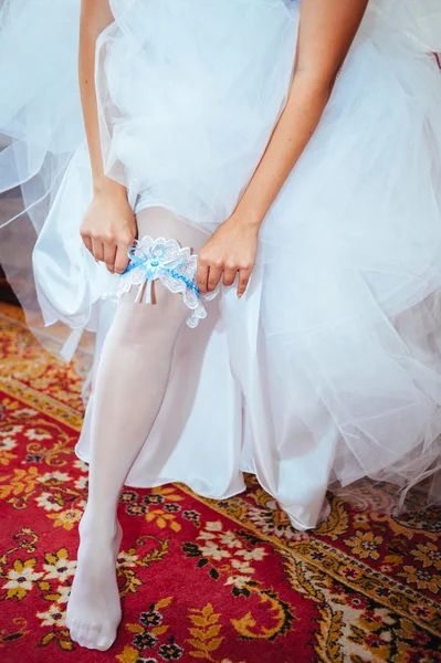 Подвязка на ноге невесты, стройная сексуальная невеста в роскошном свадебном платье, показывающая свою шелковую подвязку с золотой лентой. женщина имеет окончательную подготовку к свадебной церемонии. Моменты в день свадьбы — стоковое фото