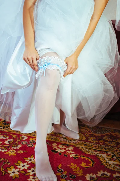 Jarretière sur la jambe de la mariée, mariée sexy mince en robe de luxe nuptiale montrant sa jarretière en soie avec ruban doré. femme ont la préparation finale pour la cérémonie de mariage. Moments de mariage — Photo