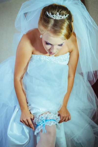 Подвязка на ноге невесты, стройная сексуальная невеста в роскошном свадебном платье, показывающая свою шелковую подвязку с золотой лентой. женщина имеет окончательную подготовку к свадебной церемонии. Моменты в день свадьбы — стоковое фото