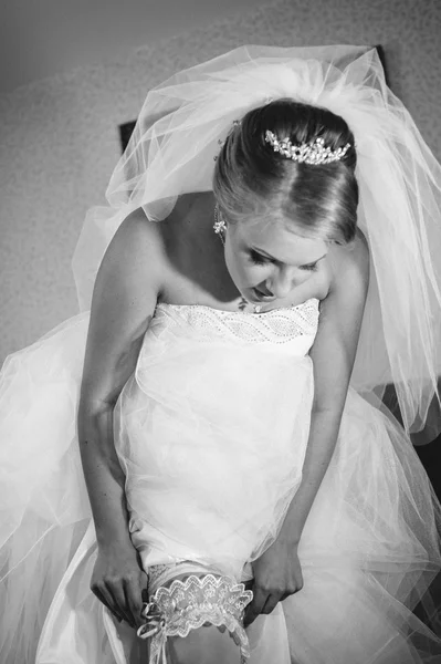 Jarretera en la pierna de la novia, novia sexy delgada en vestido de lujo nupcial que muestra su liga de seda con cinta dorada. mujer tiene la preparación final para la ceremonia de la boda. Momentos de boda —  Fotos de Stock