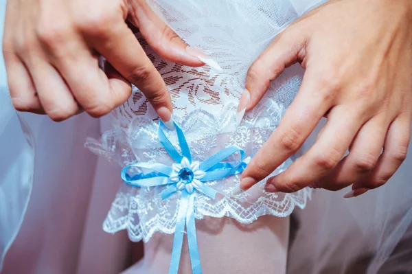 Jarretera en la pierna de la novia, novia sexy delgada en vestido de lujo nupcial que muestra su liga de seda con cinta dorada. mujer tiene la preparación final para la ceremonia de la boda. Momentos de boda — Foto de Stock