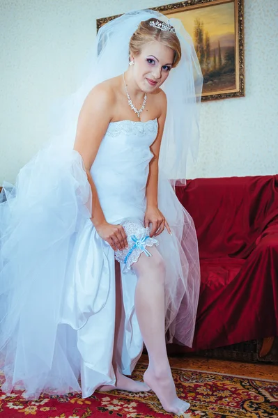 Garter on leg of bride, slim sexy bride in bridal luxury dress showing her silk garter with golden ribbon. woman have final preparation for wedding ceremony. Wedding day moments — Stock Photo, Image