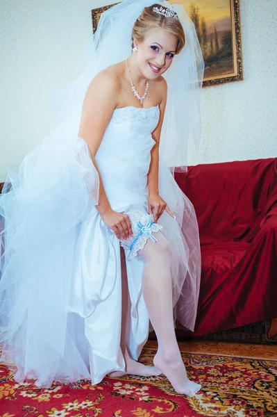 Jarretière sur la jambe de la mariée, mariée sexy mince en robe de luxe nuptiale montrant sa jarretière en soie avec ruban doré. femme ont la préparation finale pour la cérémonie de mariage. Moments de mariage — Photo