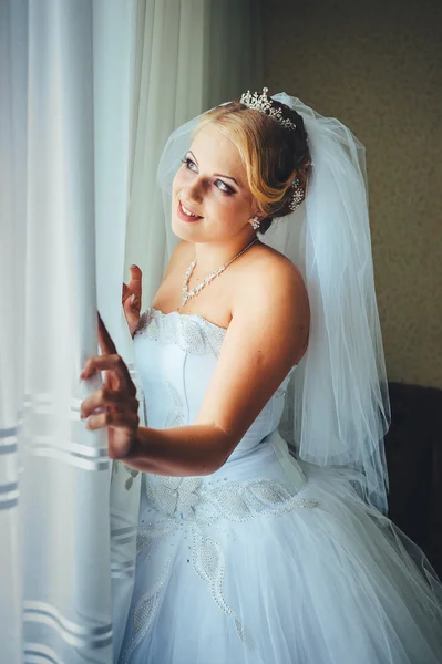 Beautiful young bride standing beside a large window waiting — Stock Photo, Image