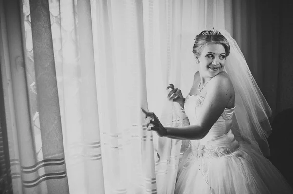 Beautiful young bride standing beside a large window waiting — Stock Photo, Image
