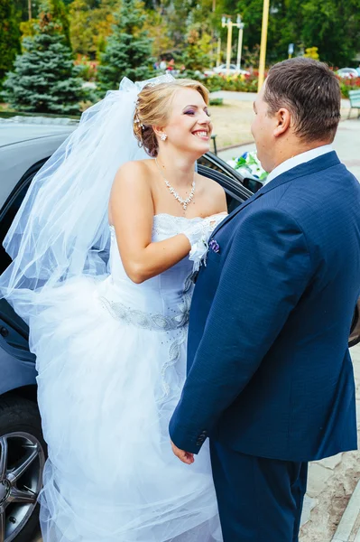 Happy groom helping his bride out of the wedding car. — Stock Photo, Image