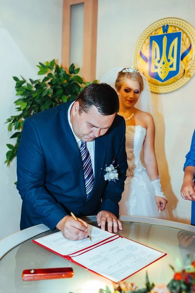 Une cérémonie de mariage. Bureau du greffe. Un couple nouvellement marié signe le document de mariage.Jeune couple signant les documents de mariage — Photo