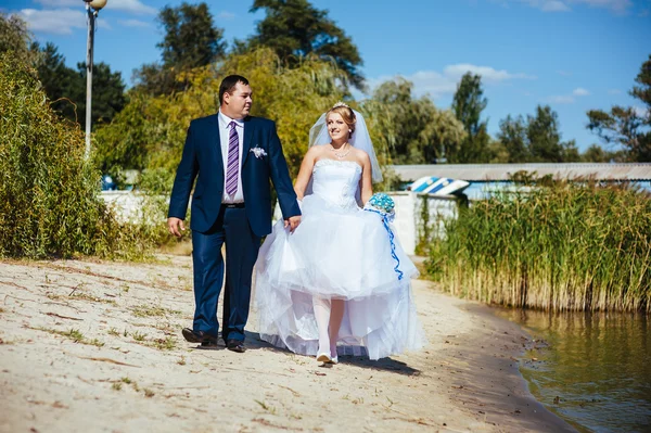 Liebendes Hochzeitspaar geht und küsst sich am Wasser — Stockfoto
