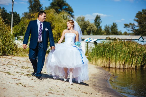 Loving wedding couple walking and kissing near water — Stock Photo, Image