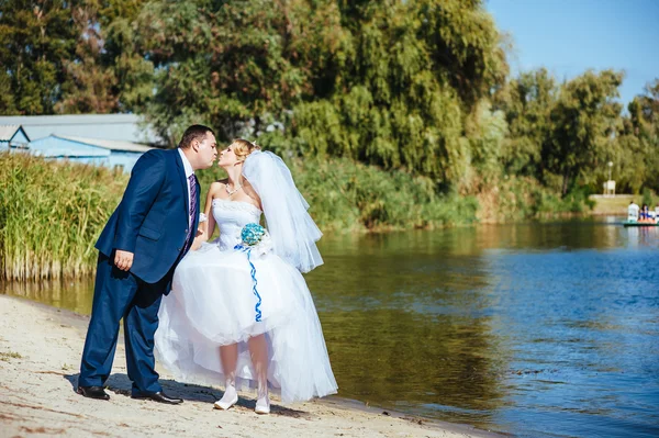 Loving wedding couple walking and kissing near water — Stock Photo, Image