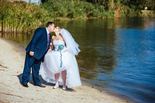 Loving wedding couple walking and kissing near water — Stock Photo, Image