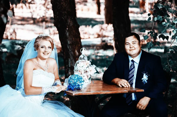 Bruden och brudgummen på sin bröllopsdag, sitter vid bord med brudbuketten. — Stockfoto