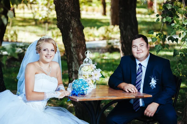 Bruden och brudgummen på sin bröllopsdag, sitter vid bord med brudbuketten. — Stockfoto