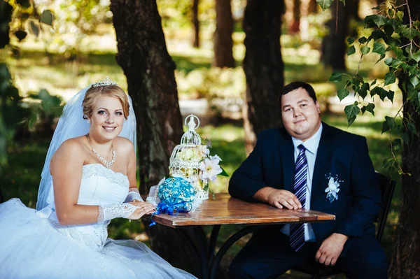 The bride and groom on their wedding day, sitting at  table with the bridal bouquet. — Stock Photo, Image