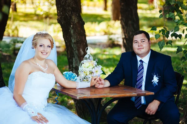 La novia y el novio en el día de su boda, sentado a la mesa con el ramo de novia . — Foto de Stock