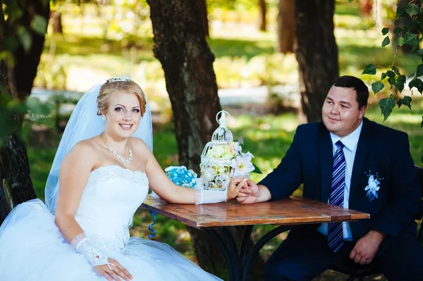 The bride and groom on their wedding day, sitting at  table with the bridal bouquet. — Stock Photo, Image