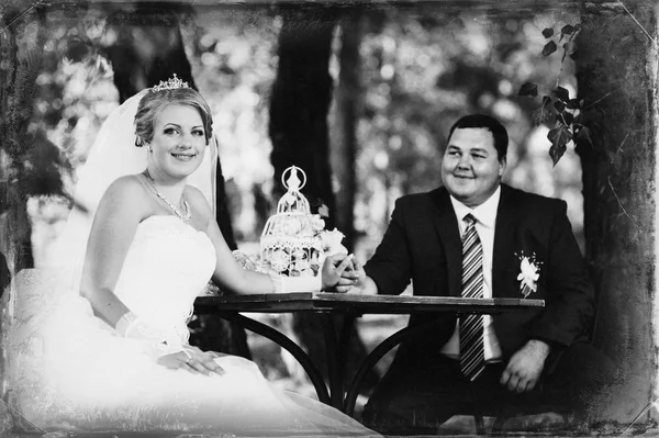 La novia y el novio en el día de su boda, sentado a la mesa con el ramo de novia . — Foto de Stock