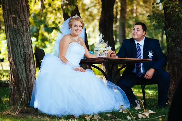 La novia y el novio en el día de su boda, sentado a la mesa con el ramo de novia . — Foto de Stock