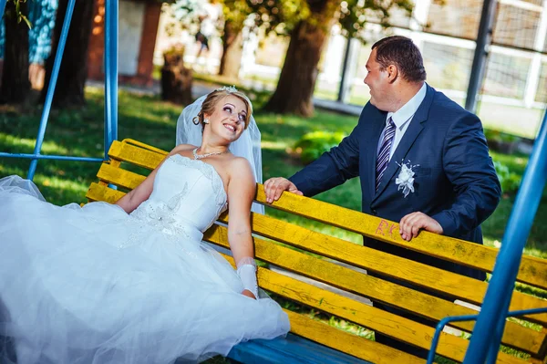 Happy bride and groom swinging on a swing in the park — Stock Photo, Image