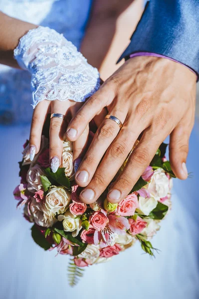 Hands of bride and groom with rings on wedding bouquet. — Stock Photo, Image