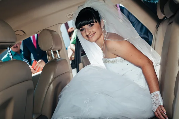 Gelukkige bruid zitten in limousine houd bloemboeket — Stockfoto