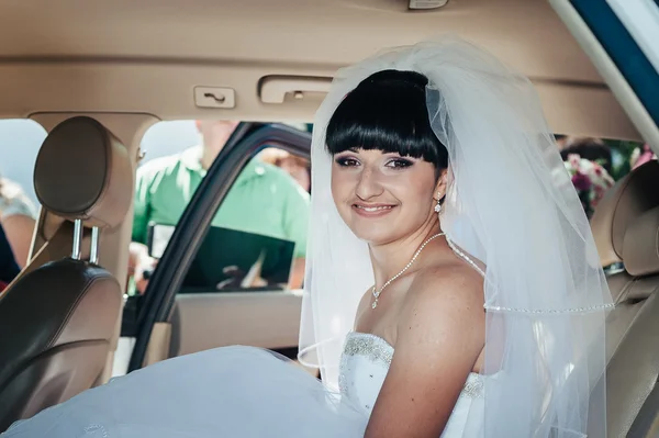 Gelukkige bruid zitten in limousine houd bloemboeket — Stockfoto