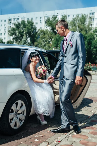 Gelukkige bruidegom zijn bruid uit de bruiloft auto helpen — Stockfoto