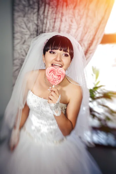 Portrait of a young bride with a heart-shaped candy lollipop — Stock Photo, Image