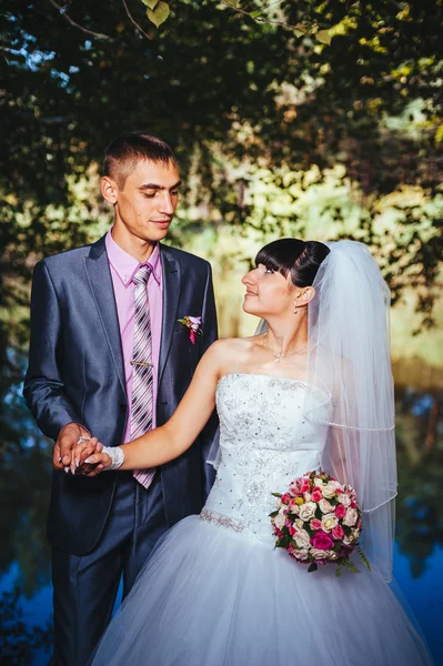 Novia y novio en el día de la boda caminando al aire libre en la naturaleza de primavera. Pareja nupcial, feliz mujer recién casada y hombre abrazándose en el parque verde. Amar pareja de boda al aire libre — Foto de Stock