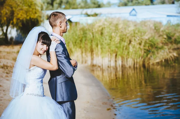 Manželský pár líbání na pláži řeka. Nevěsta ženich Svatební pár chůze venku na rivershore — Stock fotografie