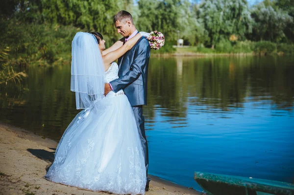 Cuplu căsătorit sărutându-se pe plaja râului. Mireasa Mire cuplu nunta de mers pe jos în aer liber pe malul râului — Fotografie, imagine de stoc