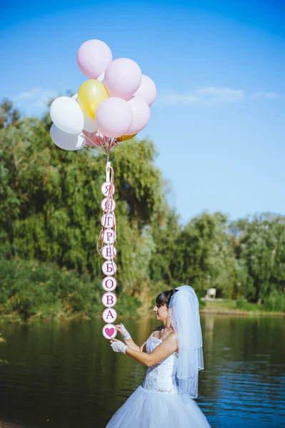 Happy young girl with big colorful latex balloons on seaside. Beauty Romantic Girl Outdoors. Woman  with long blond wavy hair  having fun on a lamppost on the background of blue sky. — Stock Photo, Image