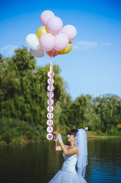 Šťastná mladá dívka s velkým barevné latexové balónky na pobřeží. Krása romantická dívka venku. Žena s dlouhé blond vlnité vlasy baví na ulici na pozadí modré oblohy. — Stock fotografie