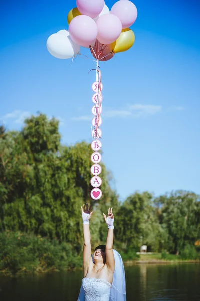 Happy young girl with big colorful latex balloons on seaside. Beauty Romantic Girl Outdoors. Woman  with long blond wavy hair  having fun on a lamppost on the background of blue sky. — Stock Photo, Image