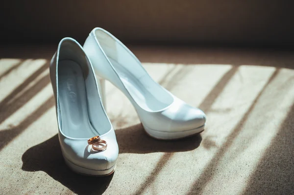 Dois anéis de ouro que colocam em sapatos de noiva de casamento branco — Fotografia de Stock