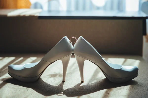 Due anelli d'oro che posano su scarpe da sposa bianche — Foto Stock