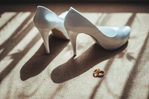 Két arany gyűrű, fehér esküvői cipőn. — Stock Fotó