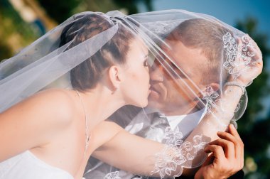 Gelin ve damat öpüşme çiçek buketi elinde tutan peçe altında